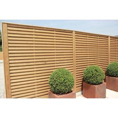 three planters are lined up next to a wooden slatted fence with plants in them