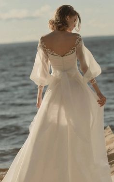 a woman in a wedding dress is standing on the rocks by the water with her back to the camera