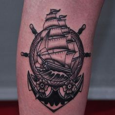 a black and white photo of a ship in a circle tattoo on the calf's leg