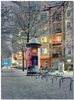 there is a snow covered street with benches and a light pole in the foreground