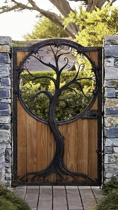 an iron gate with a tree design on the top and bottom part, in front of a stone wall