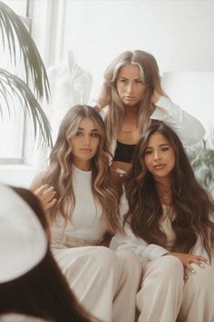 three beautiful women sitting next to each other in front of a window with palm trees