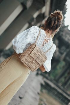 a woman with a white top and tan pants is holding a straw bag in front of an old building