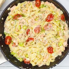 a skillet filled with pasta and vegetables on top of a white table next to utensils