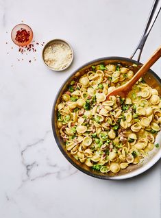 a skillet filled with pasta and vegetables on top of a white marble countertop