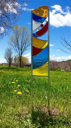 a colorful glass sculpture in the middle of a grassy field with trees and blue sky behind it