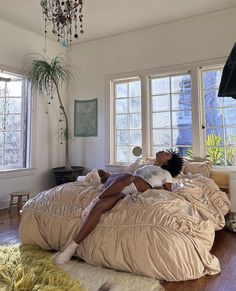 a woman laying on top of a bed in a bedroom next to two large windows