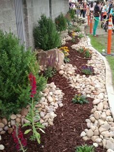 a garden with rocks and flowers in the grass next to a building at an outdoor event