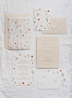 the wedding stationery is laid out on a white sheet with floral designs and envelopes