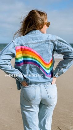 a woman standing on the beach with her back to the camera and wearing a jean jacket