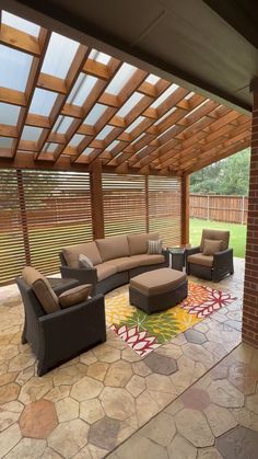 an outdoor living area with couches, chairs and a rug on the floor under a pergolated roof