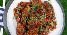 a white plate topped with chicken wings covered in sauce and garnished with herbs