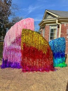 two large colorful sculptures in front of a brick house with blue sky and clouds behind them