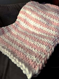 a pink and white crocheted blanket sitting on top of a couch