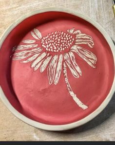 a red bowl with a flower painted on it next to a pen and paper clip