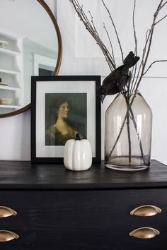 a black dresser topped with a glass vase filled with flowers and a bird sitting on top of it