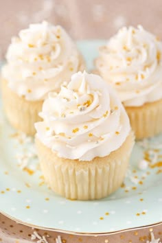 three cupcakes with white frosting and gold sprinkles on a plate