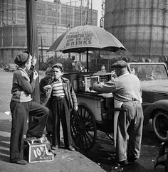 an old black and white photo of three people selling food from a cart on the street