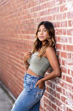 a beautiful young woman leaning against a brick wall