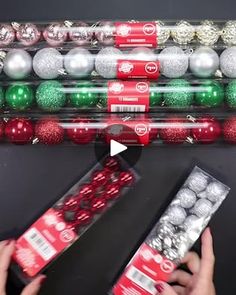 two hands are holding christmas balls in front of a display case filled with other ornaments