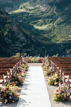 an outdoor ceremony setup with wooden chairs and flower arrangements on the aisle, overlooking mountains