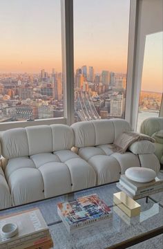 a white couch sitting in front of a window next to a table with books on it