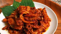 a white plate topped with meat covered in sauce and garnished with green leaves