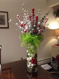 a glass vase filled with candy canes and greenery on top of a wooden table