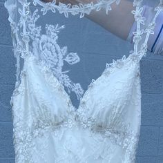 a woman wearing a white wedding dress with lace on the top and bottom, standing in front of a brick wall