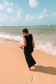 a woman is walking on the beach with her shoes in hand and looking at the water