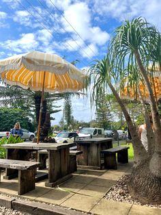 two picnic tables under an umbrella on the side of the road with cars parked in the background