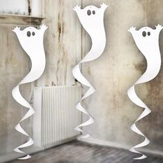 three white paper hangings in the shape of ghost faces on a wall next to a radiator