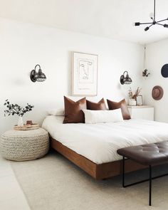 a white bed with brown pillows in a bedroom next to a plant on the wall