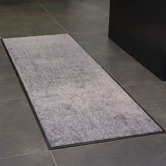 a white rug on the floor in a room with tile floors and black furniture behind it