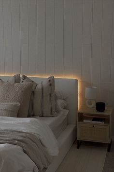 a bed with white sheets and pillows in a bedroom next to a night stand that has lights on it