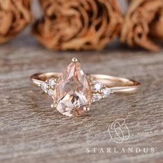 a pink diamond ring sitting on top of a wooden table next to some dried flowers