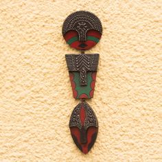 two african masks are hanging on the side of a wall, one is red and green