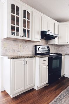 an empty kitchen with white cabinets and black stove top oven, wood flooring and hardwood floors