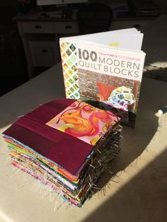 a stack of quilt blocks sitting on top of a table next to a book titled 100 modern quilt blocks