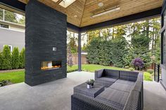 an outdoor fireplace in the middle of a covered patio area with furniture and large windows