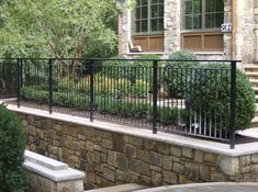 a black iron fence on the side of a stone wall next to trees and bushes