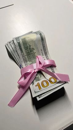 a bunch of money is tied up on top of a desk with a pink ribbon