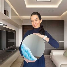 a woman holding up a round mirror in her living room with a couch and television on the wall