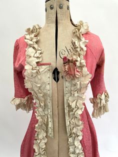 "This rare and absolutely lovely antique late Victorian over dress is made from pink figured silk with cream figured silk highlights at the bodice. The edges of the pink silk fabric are trimmed with delightful ruffled cream coloured silk and the sleeve ends are trimmed with ruffled silk and lace. There is a beautiful flower corsage to the left hand side of the bodice. The inside of the bodice is boned with what looks to be steel and is lined with cotton. The design of the dress has swags of fabric to each side which falls beautifully when it is displayed on a mannequin/dress form, as does the back of the dress which has a full-length central pleat. This would be a lovely addition to a collection of antique clothing.  It has an interior label for the department store George Henry Lee and Co Pink Fitted Rococo Victorian Dress, Pink Victorian Dress With Historical Design For Wedding, Vintage Pink Costume Dresses, Pink Fitted Victorian Marie Antoinette Dress, Pink Fitted Victorian Dress Marie Antoinette Style, Pink Rococo Victorian Dress, Pink Victorian Wedding Dress With Historical Design, Pink Victorian Rococo Dress For Costume, Victorian Style Pink Costume Dress