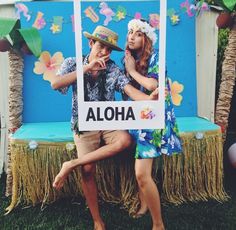 a man and woman pose for a photo in front of a sign that says aloha