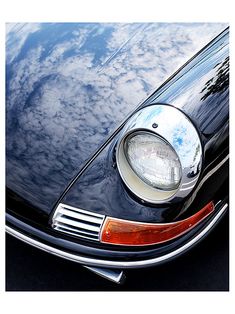 the front end of a black car with clouds in the background