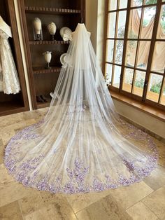 a wedding veil is on display in a bridal room with purple flowers all over the floor