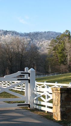 a white fence with a stone pillar and gate in front of a grassy field on a sunny day