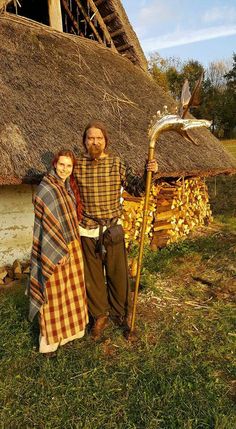 a man and woman standing next to each other in front of a thatched house