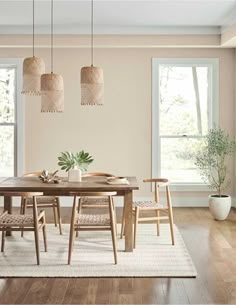 a dining room table and chairs in front of two large windows with wooden flooring